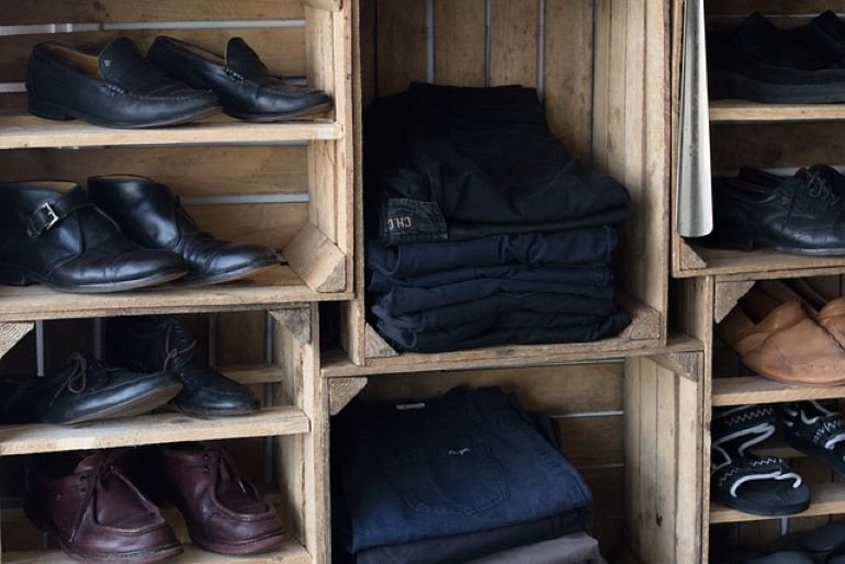 Various shoes and folded pants are neatly arranged on wooden shelves.