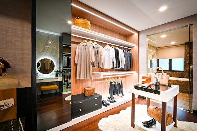 Modern walk-in closet design featuring open shelving, hanging clothes, accessories, a vanity table, and elegant lighting